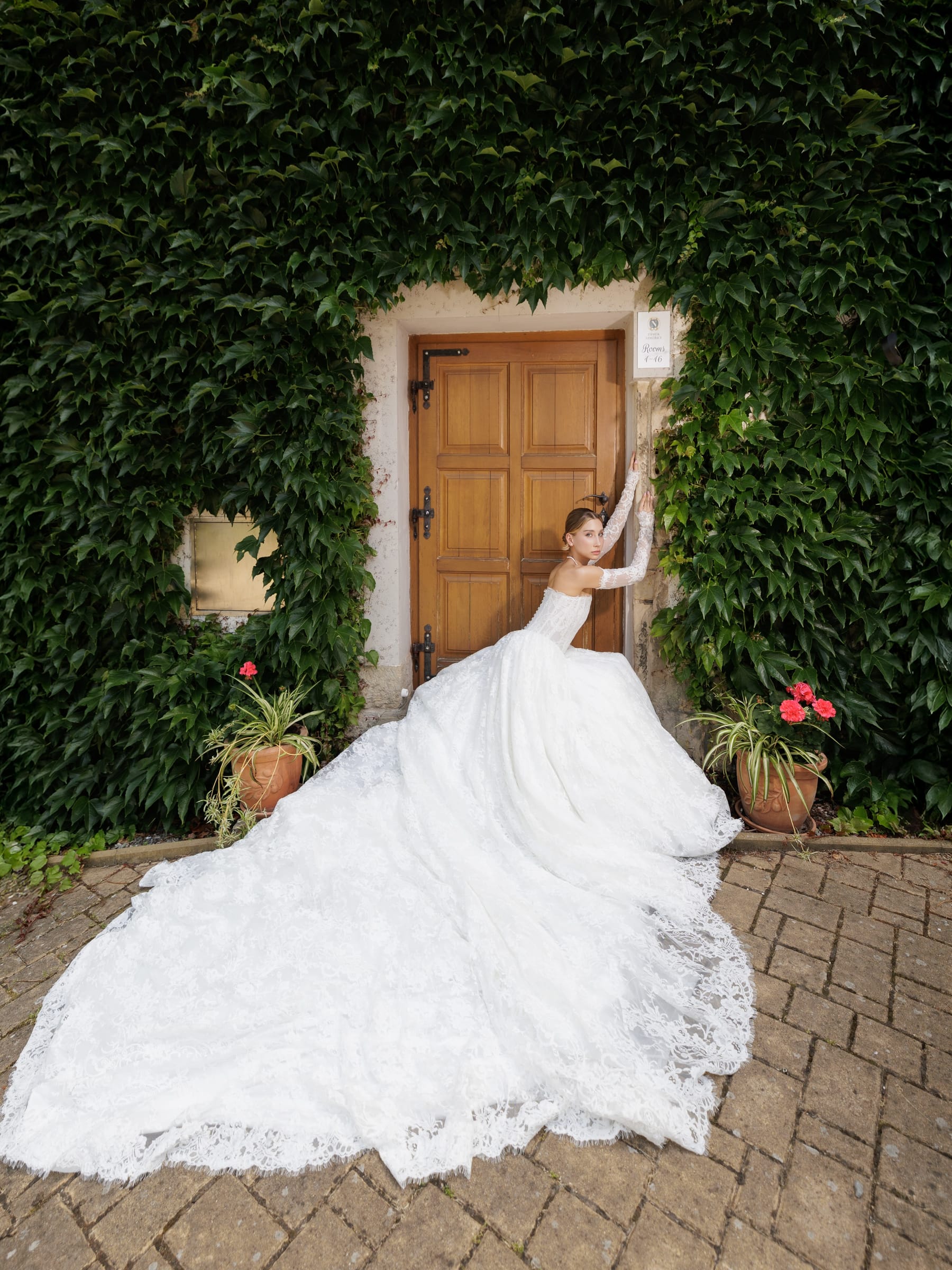 Full-length photograph from Lidiia Krejci Wedding Salon: a model in a fitted strapless white gown, one hand raised to her hair.
